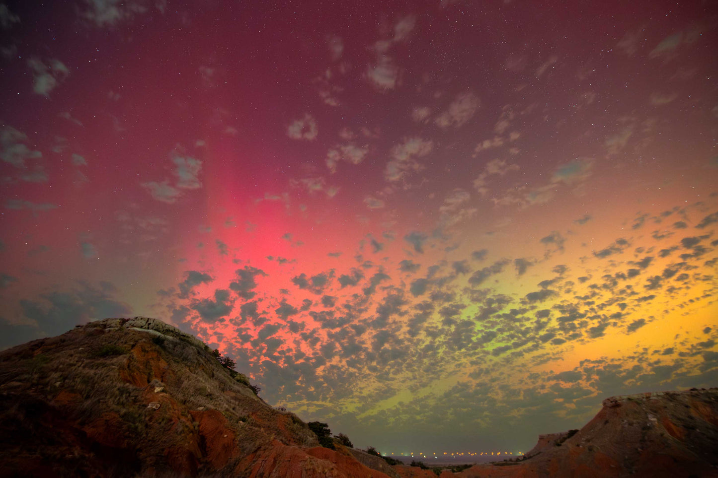 Rainbow aurora over red dirt mesas.